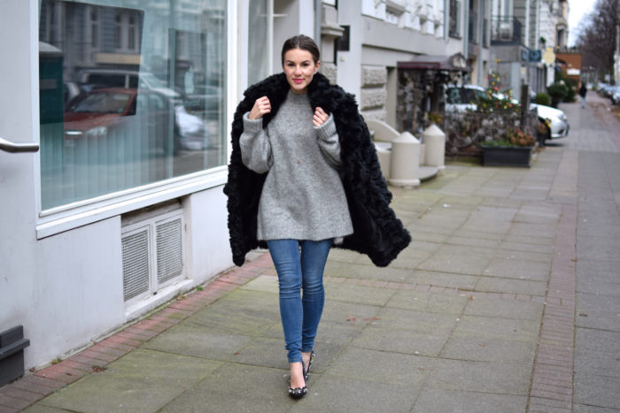 Schwarzer Kuschelmantel, Teddy, grauer Strickpullover, Jeans, Pumps