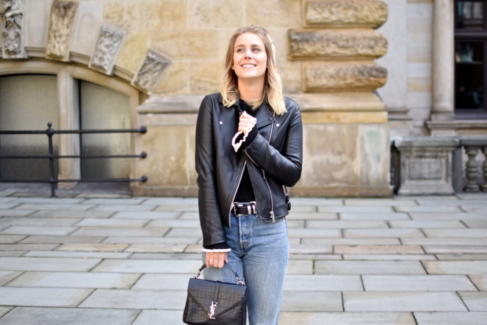 smile, leather biker jacket, jeans and belt, black bag