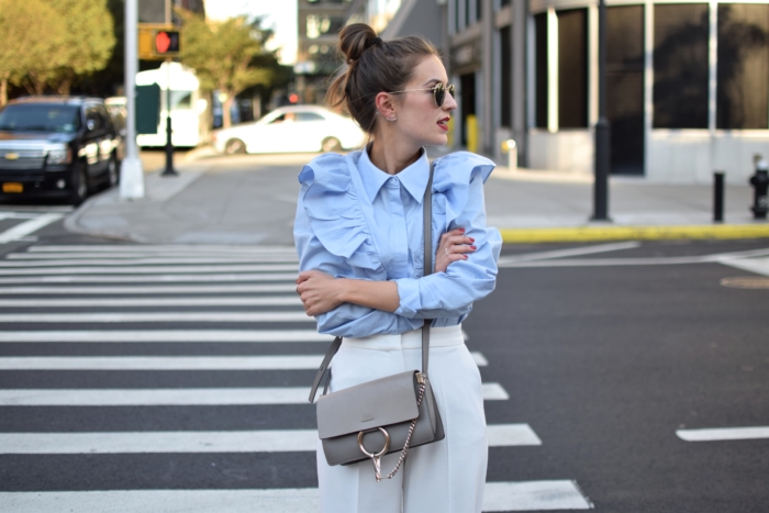 Rüschenbluse blau, weiße Hose, graue Handtasche, Sonnenbrille