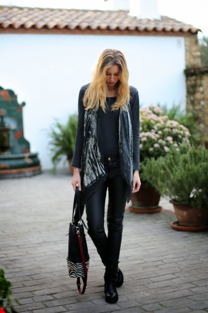 Blondes Model mit grauem Top, schwarzer Hose, gemustertem Schal und schwarzen Boots