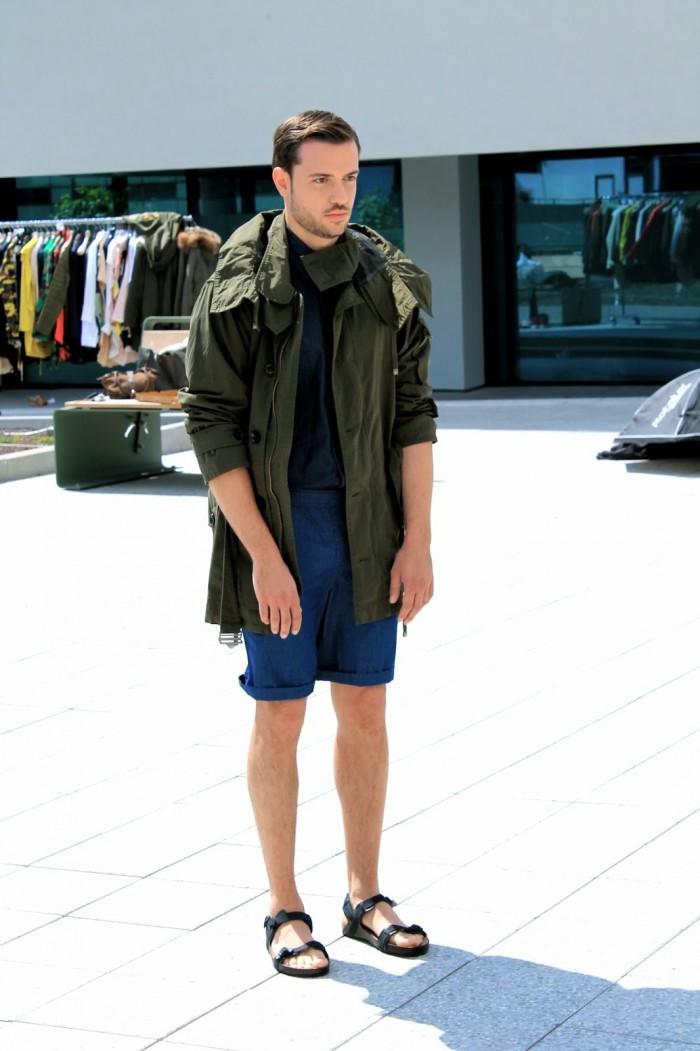 Männliches Model mit grünem Parka und blauen Shorts